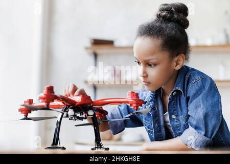 Giovane ragazza carina che tiene quadcopter. Bambino che gioca con drone a casa. Istruzione, studio domestico, bambini, tecnologia, scienza, futuro, concetto di persone Foto Stock