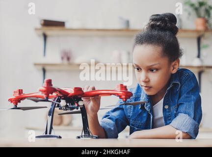 Giovane ragazza carina che tiene quadcopter. Bambino che gioca con drone a casa. Istruzione, studio domestico, bambini, tecnologia, scienza, futuro, concetto di persone Foto Stock