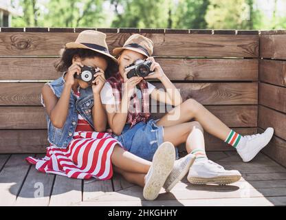 Bambini amici che giocano insieme all'aperto. Belle bambine che scattano foto con le fotocamere. Divertimento estivo, concetto di vacanze Foto Stock