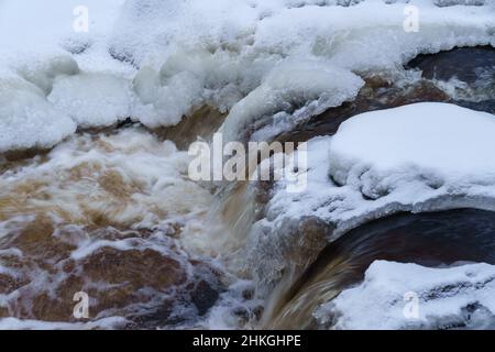 Fiume non ghiacciato in una foresta innevata in un'oscura e fredda giornata invernale Foto Stock