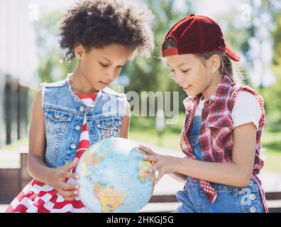 Ragazze piccole felici che guardano il globo, l'istruzione o concetto di viaggio Foto Stock