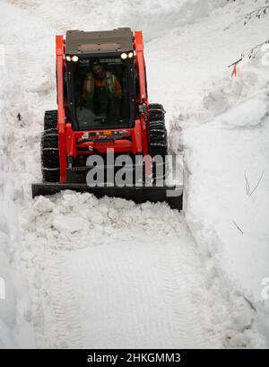 Piccolo spazzaneve che muove la neve sul sentiero come visto dall'alto con catene sugli pneumatici invernali dopo una tempesta di neve nel piccolo villaggio sciistico della Columbia Britannica Foto Stock