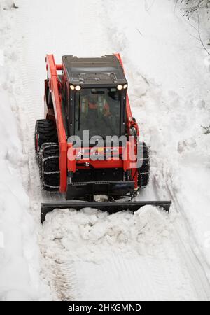 Piccolo spazzaneve che muove la neve sul sentiero come visto dall'alto con catene sugli pneumatici invernali dopo una tempesta di neve nel piccolo villaggio sciistico della Columbia Britannica Foto Stock