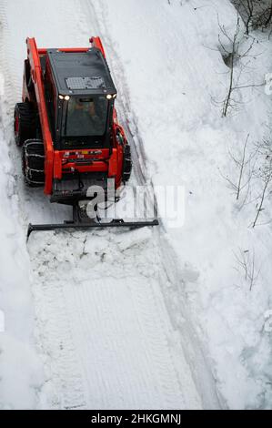 Piccolo spazzaneve che muove la neve sul sentiero come visto dall'alto con catene sugli pneumatici invernali dopo una tempesta di neve nel piccolo villaggio sciistico della Columbia Britannica Foto Stock