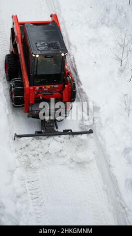 Piccolo spazzaneve che muove la neve sul sentiero come visto dall'alto con catene sugli pneumatici invernali dopo una tempesta di neve nel piccolo villaggio sciistico della Columbia Britannica Foto Stock