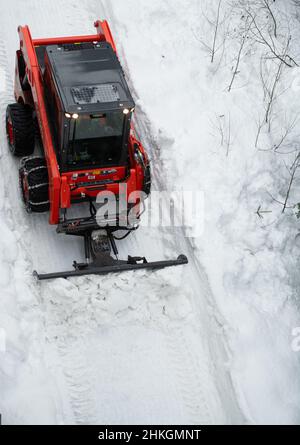Piccolo spazzaneve che muove la neve sul sentiero come visto dall'alto con catene sugli pneumatici invernali dopo una tempesta di neve nel piccolo villaggio sciistico della Columbia Britannica Foto Stock