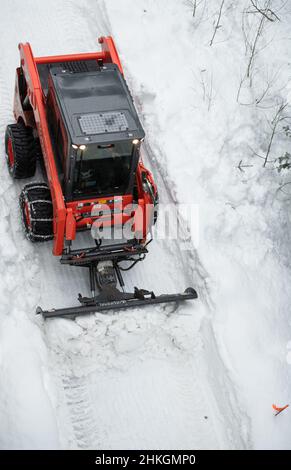 Piccolo spazzaneve che muove la neve sul sentiero come visto dall'alto con catene sugli pneumatici invernali dopo una tempesta di neve nel piccolo villaggio sciistico della Columbia Britannica Foto Stock