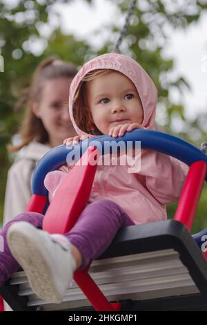 Ragazza caucasica di 2 anni che gioca su un parco giochi, divertirsi oscillando su un altalena Foto Stock