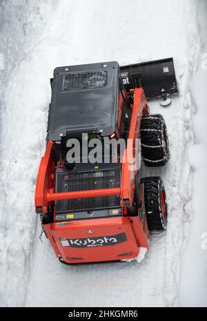 Piccolo spazzaneve che muove la neve sul sentiero come visto dall'alto con catene sugli pneumatici invernali dopo una tempesta di neve nel piccolo villaggio sciistico della Columbia Britannica Foto Stock