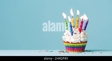 Cupcake di compleanno con un sacco di candele di compleanno colorate su uno sfondo blu con spazio copia a lato Foto Stock