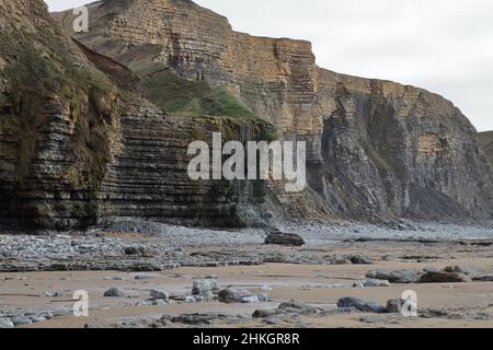 Guardando verso sud dalla baia di Dunraven con la cascata Magica che scorre dolcemente sulla cima della scogliera e giù sulla sabbia. Foto Stock