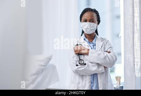 La passione nella cura della comunità. Ritratto di un giovane medico che indossa una maschera facciale e tiene uno stetoscopio in ospedale. Foto Stock