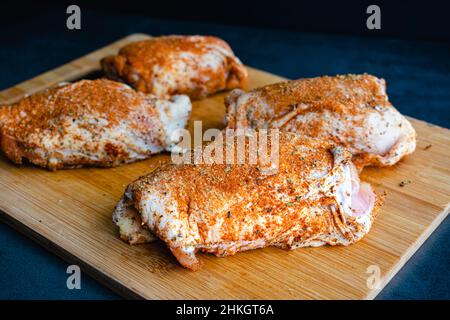 Bone-in Skin-on Raw Chicken cosce strofinate con miscela di spezie: Cosce di pollo non spice-rubbed su un tagliere di legno Foto Stock
