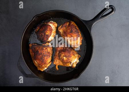 Vista dall'alto delle cosce di pollo spazzate con spezie in una zilletta di ghisa: Cosce di pollo arrostite con osso sulla pelle arrostite in una padella in ghisa Foto Stock