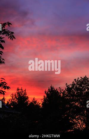 La prima luce dell'alba illumina rossi, arance e blues luminosi dipinti sulle nuvole passanti. Foto Stock