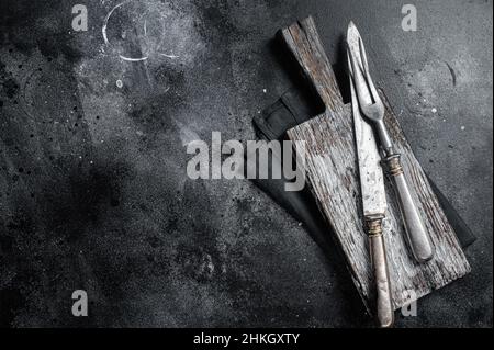 Forchetta e coltello vintage per macellaio con telo su tavola di legno. Sfondo nero. Vista dall'alto. Spazio di copia Foto Stock