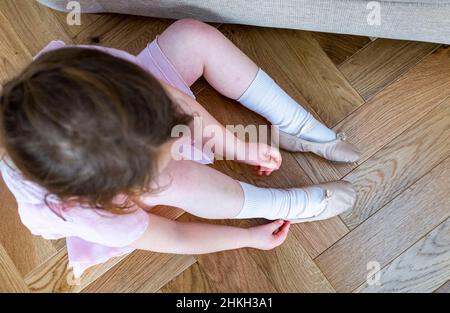 Ragazza giovane cheeky di 5 anni che mette sulle sue scarpe di balletto pronte per una classe di ballo UK Foto Stock