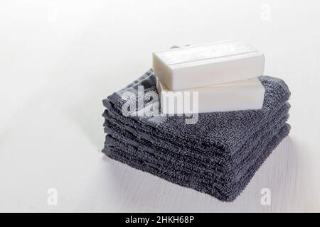 Set spa di asciugamani grigi e due pezzi di saponi su sfondo bianco in legno. Set regalo, orientamento orizzontale vista laterale. Concetto di trattamenti Spa. COP Foto Stock