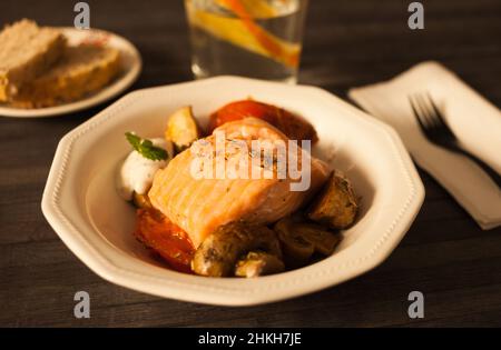 filetto di salmone al vapore su un cuscino di funghi fritti e pomodori in un recipiente bianco Foto Stock