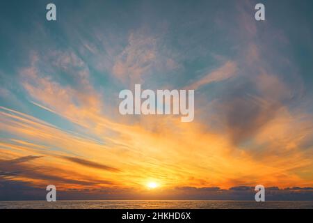 Magnifica vista delle nuvole di cirro sfocate con una luce meravigliosa e un disco solare sull'orizzonte della superficie del mare dell'acqua Foto Stock