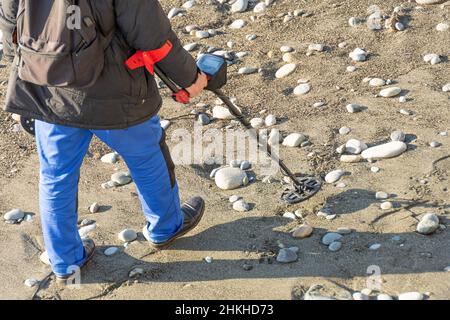 Uomo con un metal detector su una spiaggia di sabbia rocciosa dopo la tempesta Foto Stock
