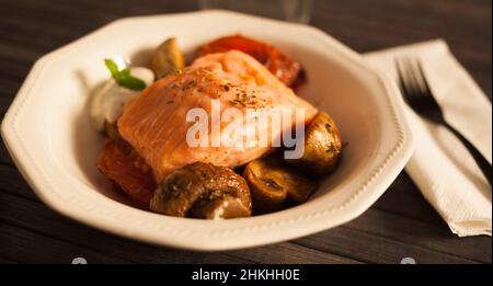 filetto di trota di mare al vapore servito su funghi fritti con pomodori in un recipiente bianco Foto Stock