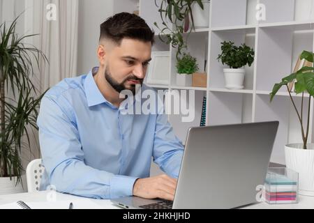 Bell'uomo lavora su un laptop in un moderno interno in remoto su Internet. Foto Stock