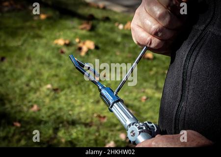 Uomo che usa il cacciavite per attaccare un attacco di presa ad un palo lungo all'aperto con erba e caduta foglie sullo sfondo - primo piano delle mani - selettivo f Foto Stock