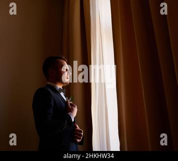 giovane uomo in camicia bianca che fissa i gemelli sulle maniche vicino alla finestra. ritratto aziendale. Lo sposo incontrerà la sposa. Matrimonio, uomo d'affari Foto Stock