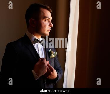 giovane uomo in camicia bianca che fissa i gemelli sulle maniche vicino alla finestra. ritratto aziendale. Lo sposo incontrerà la sposa. Matrimonio, uomo d'affari Foto Stock