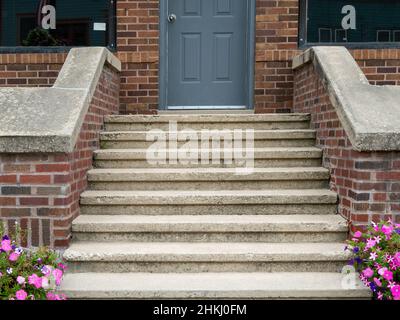 Scale di cemento che conducono ad una porta grigia in un edificio a muro di mattoni. Foto Stock