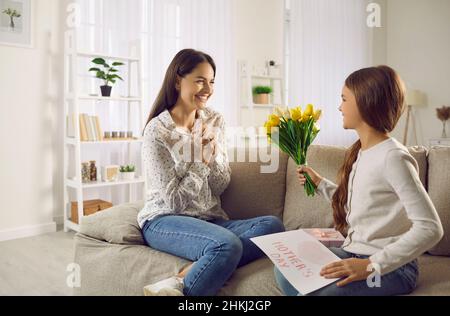 La giovane donna felice ottiene una carta e fiori dalla sua figlia piccola in festa della mamma Foto Stock