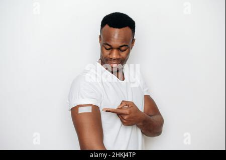 Assistenza sanitaria, covid 19, influenza. Sano sorridente giovane adulto afroamericano uomo, in piedi con una banda-aiuto sul suo braccio dopo aver ricevuto il primo vaccino per prevenire la diffusione di coronavirus malattia Foto Stock