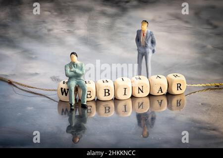 Modello in miniatura di uomini d'affari e cubetti di legno con iscrizione del webinar posta su un filo su un tavolo riflettente. Il concetto di formazione online. Foto Stock