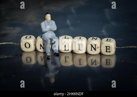 Modello in miniatura di uomo d'affari seduto su un cubi online come testo con lettere, strung su un filo. Concetto di business online. Foto Stock