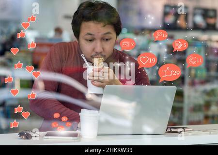 Uomo d'affari asiatico mangiando noodles con azione urgente in ore di punta e controllando l'applicazione di rete sociale con il numero di mi piace, Amore, commento, persone e Foto Stock