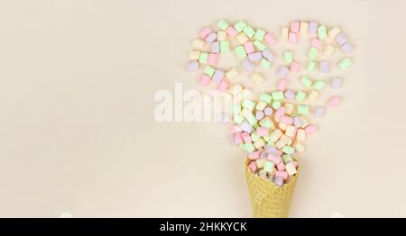 Disposizione con cornet a cono di cialda e marshmallows colorate in forma di cuore su sfondo pastello Foto Stock