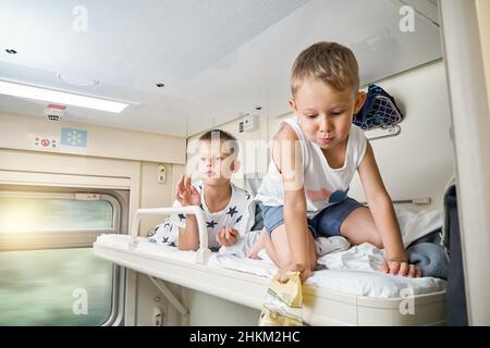 I fratelli con capelli biondi indossando abiti casual riposano e si rilassano sulla mensola superiore in treno auto e mangiare spuntini dal primo piano del pacchetto Foto Stock
