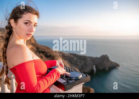 Le mani femminili del DJ suonano la musica mescolando e graffiando durante la festa serale con sfondo marino e caldo tramonto morbido. Primo piano di una console DJ controllata da Foto Stock