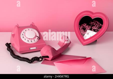 Telefono retrò con specchio a cuore e buste al tavolo. Ancora vita in colore rosa. Concetto di giorno di San Valentino. Foto di alta qualità Foto Stock