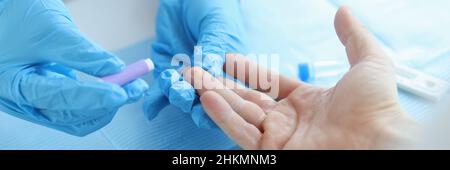 Il medico glovered prende l'esame del sangue con la lancetta dal paziente alla clinica Foto Stock