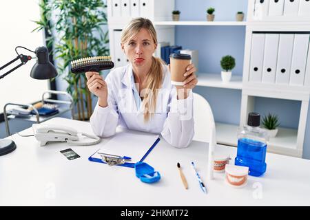 Bella donna dentista che tiene la dentiera e spazzolino depressi e preoccuparsi per il disagio, piangendo arrabbiato e paura. Espressione triste. Foto Stock