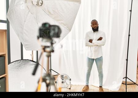 L'uomo afroamericano che posa come modello allo studio di fotografia scettico e nervoso, disapprovando l'espressione sul viso con le braccia incrociate. Persona negativa. Foto Stock