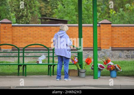 Una donna anziana vende fiori ad una fermata dell'autobus nella città, Ucraina. Il lavoro autonomo degli anziani, i problemi della povertà. Foto Stock