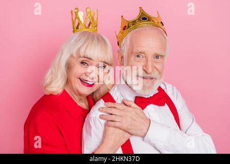 Ritratto di attraente coppia grigio-capelli allegra indossando tiara abbraccio isolato su sfondo rosa pastello colore Foto Stock