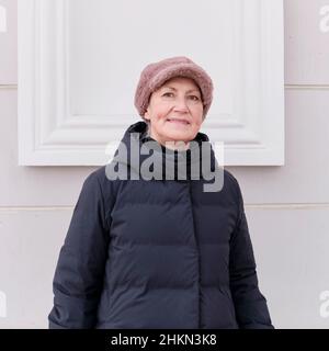 Ritratto invernale di donna anziana sorridente che guarda la macchina fotografica, con cappuccio in pelliccia rosa sintetica. Foto Stock