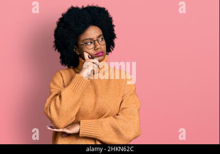 Giovane donna afroamericana che indossa abiti casual faccia seria pensare alla domanda con la mano sul mento, pensieroso circa idea confusa Foto Stock