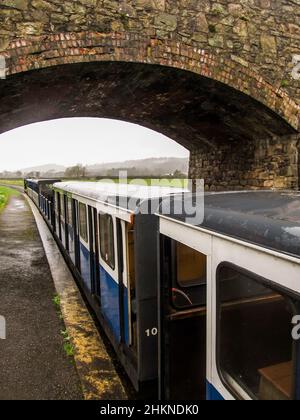 Un piccolo treno turistico diesel, sotto un ponte sulla ferrovia del patrimonio tra Ravenglass ed Eksdale nel Lake District, Regno Unito Foto Stock