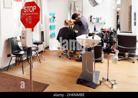 Berlino, Germania. 05th Feb 2022. Il parrucchiere Noor Agha Karimi fa i capelli di un cliente al salone dei capelli del Mac a Wannsee. In salone si trova un cartello con la richiesta di disinfettare le mani. In vista dell'ondata di Omikron, il Senato di Berlino ha adottato alcune nuove regole di Corona. Il regolamento è in vigore dal 05.02.2022. Credit: Carsten Koall/dpa/Alamy Live News Foto Stock