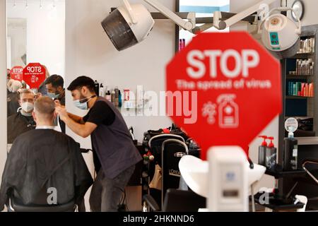 Berlino, Germania. 05th Feb 2022. Il parrucchiere Noor Agha Karimi fa i capelli di un cliente al salone dei capelli del Mac a Wannsee. In salone si trova un cartello con la richiesta di disinfettare le mani. In vista dell'ondata di Omikron, il Senato di Berlino ha adottato alcune nuove regole di Corona. Il regolamento è in vigore dal 05.02.2022. Credit: Carsten Koall/dpa/Alamy Live News Foto Stock